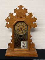 Front view of the antique mantle clock showing the wooden gingerbread style case with intricate cut-out design and octagonal clock face frame.