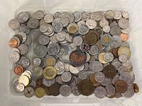 Wide view showing mixed quantity of world coins in a container, featuring various countries and materials including copper, silver tones and bimetallic coins.