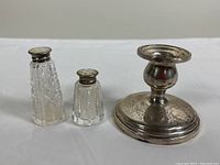 Photo showing the two crystal salt and pepper shakers with sterling silver mother of pearl lids and the weighted sterling silver candleholder with tarnishing and small dents.