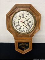 Full view of the wooden octagonal pendulum mantle clock showing wood frame, glass front with Standard Time label, and clock face.