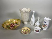 Wide shot showing six bone china items including floral bowls, vases, a dish and the toothpick holder arranged on a gray background.