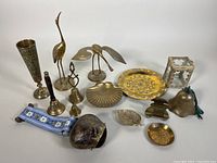 Full group view of all brassware items including crane statues, bells, plates, ashtray, and tin, arranged on white background