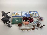Wide view of lot showing miniatures including Czech glass elephant, brass statue corkscrew, pewter pelican, red glass animals, tile trivets, and assorted small figurines.