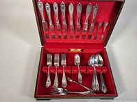 Full set displayed in open chest showing spoons, forks, knives and teaspoons in red velvet-lined wooden chest.
