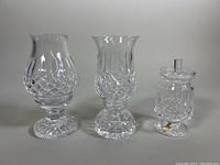 Three cut crystal pieces: a footed honey/condiment dish on the right, two two-piece hurricane candle holders on the left, showing intricate diamond cut pattern and overall shape.