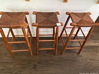 Front view of three brown wicker bar stools showing the woven seats and wooden legs.