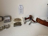 Photo showing oval and rectangular cowboy belt buckles on a white cloth next to the spurs and leather holster belt.