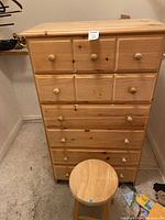 Front view of the pine dresser and round stool placed in front of it, showing 6 drawers with wood knobs.