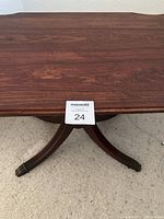 Close-up of one of the splayed legs with metal claw foot and part of the table leg and top surface with wood grain detail.