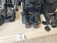 Four pairs of binoculars placed side by side showing carrying cases and lens caps in black color.