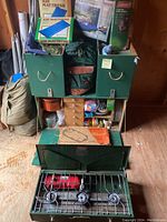 Photo showing the green custom storage cabinet with cubbies, sleeping air mattresses, a green backpack, and the Coleman stove set up at the front.
