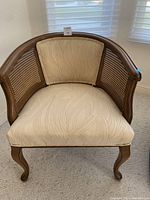 Front view of the round back wooden chair with beige upholstered seat and cushion, showing curved legs and cane panel sides.