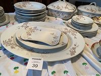 Wide view of varied china plates, bowls, serving dishes with brown floral pattern on white.
