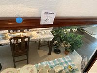 Close view of the wooden frame on the top edge of the mirror showing the finish and style, positioned horizontally on the wall above a dining room setting.