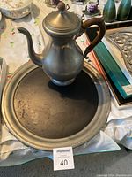 Teapot with wooden handle on a round metal tray; shows patina and wear on tray.