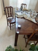 View showing wooden dining table with parquet pattern top and carved legs, five matching chairs with top seat pads around it.