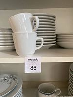 Photo of stacked white coffee cups and small plates on a shelf