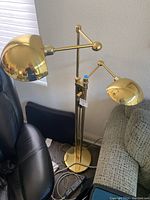 Full view of dual-head brass floor lamp positioned between chair and sofa