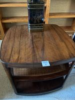 Photo of the wooden end table showing the smooth brown finish top and two lower shelves including a woven shelf insert.