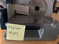 Front view of the kitchen meat slicer showing the blade, food carriage, and a MaxSold sticky note with the lot number.