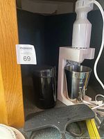 White hand mixer with stainless steel mixing cup and black coffee grinder on shelf