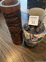 Two vases side by side, one carved wood and one ceramic with painted design.