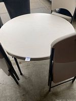 Top view of the 46-inch round beige resin tabletop with four black metal legs visible around it, showing table surface and legs.