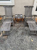 Front view of two aged teak lounge chairs with footrests and small table between them