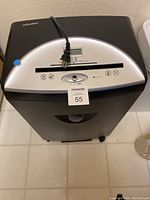 Front top view of the silver control panel, showing paper slot, control buttons, and digital display with power cord resting on top.