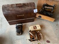 Wide view of vintage Singer sewing machines with curved wooden case, antique hair trimmer, power cord, and boxed soap.