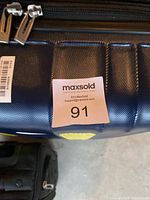 Close-up of blue hard shell suitcase showing zipper pulls, textured surface, and MaxSold sticker