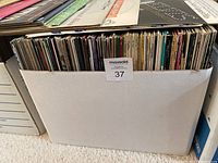 Photo showing 3 banker boxes filled with vinyl record albums placed on the floor, top edges of records visible