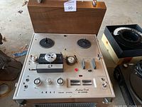 Photo of Akai reel to reel tape recorder with wood case cover open, showing dials and controls.