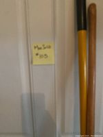 Photo of a hatchet with yellow and black handle alongside a wooden handle tool against a door with a sticky note labeled 'Max Sold #105'.