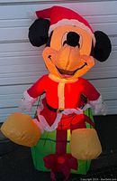 Front view of the inflatable Mickey Mouse dressed as Santa Claus sitting on a gift box.