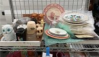 Wide view showing multiple plates stacked, including some wrapped with bubble wrap, and animal-shaped ceramic pieces on metal shelving