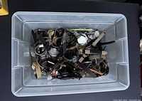 Plastic bin filled with approximately 100 assorted vintage wristwatches of various strap types, colors, and case styles.