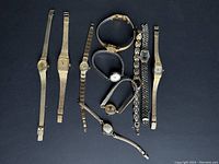 All nine vintage ladies watches laid out on black background, showing overall lot contents and condition.