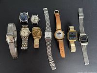 Full lot of eight vintage watches arranged in a row on black surface showing various styles, colors, and bands.