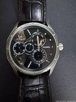 Front view of men's Fossil Twist chronograph watch showing black dial with subdials and partial skeleton detail, black leather strap with subtle wear.