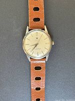 Full front view of watch mounted on brown perforated leather strap against dark background