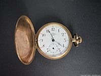 Open-pocket watch showing white dial with Arabic numerals and black and red markings.