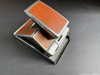 Polaroid SX-70 Land camera partially open showing brown leather panels and metal frame.