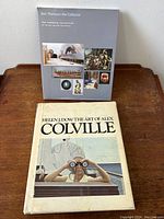 Two coffee table books placed on a wooden surface; front cover of Alex Colville book with woman holding binoculars and Ken Thomson book with art images on gray cover