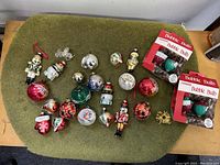 Full view of all 20 glass Christmas tree ornaments including nutcracker, snowmen, Santa, decorative bulbs, and 4 boxed NOMA bubble bulb light bulbs.