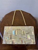 Top-down view of rectangular clutch showing mother of pearl patchwork inlay surface on gold-tone frame.