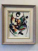 Framed oil painting showing a colorful, abstract Harlequin Pierrot figure playing guitar, signed at the bottom right.