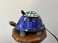 Front view of figural turtle stained glass lamp with smaller turtle on its shell, displayed on a wooden stool.