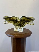 Front angle view of the green cased Chalet art glass bowl on a wooden stand, showing its organic shaped rim and clear base.