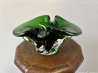 Angled side view showing the emerald green glass ashtray with thick base and organic folded edges.